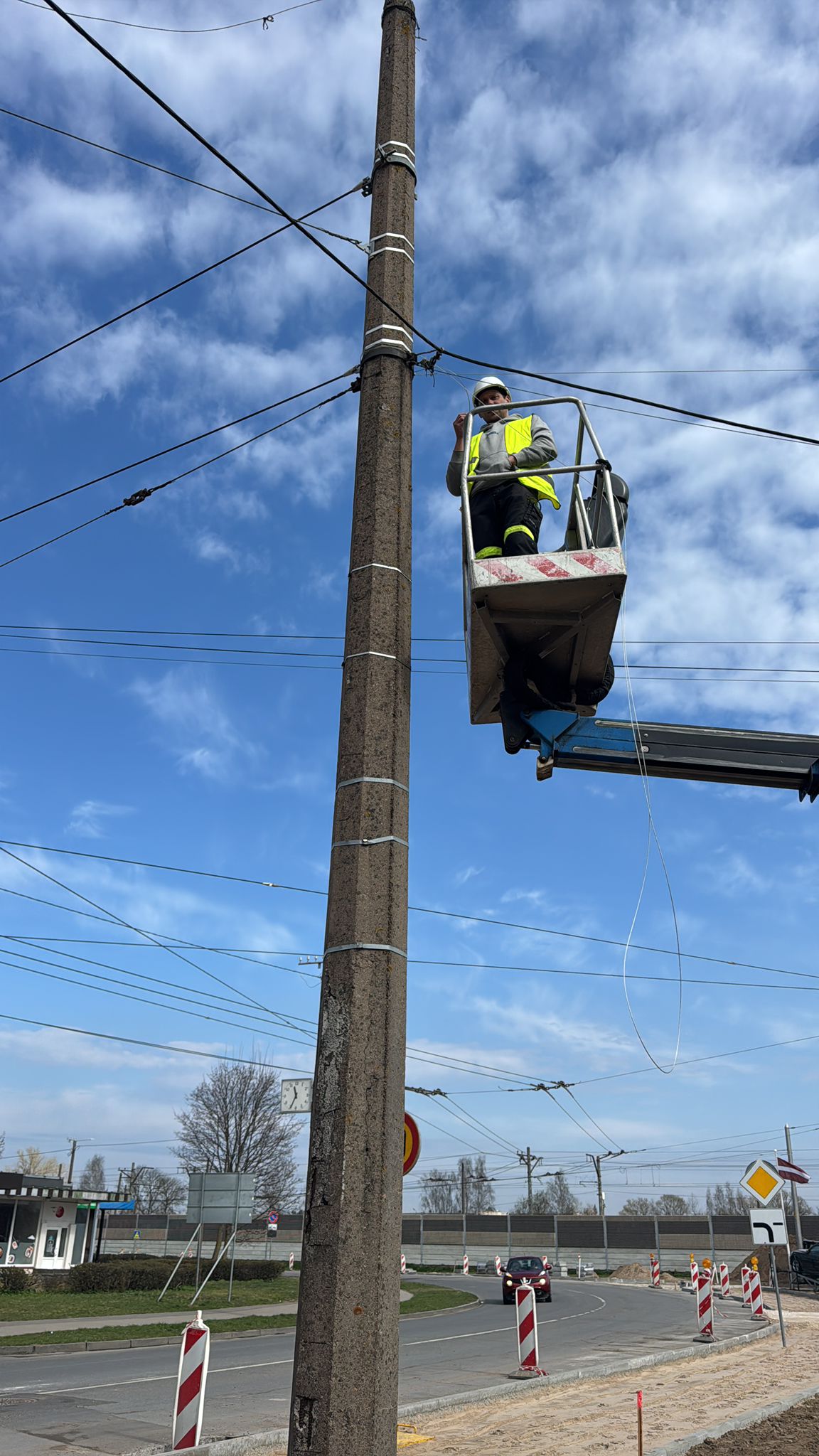 Elektriķis pacēlājā pie augsta betona staba, kabeļu apkope